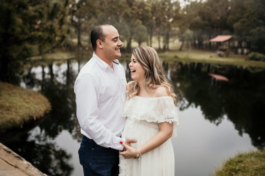 Mujer junto a su esposo somriendo en sus fotos de embarazo.