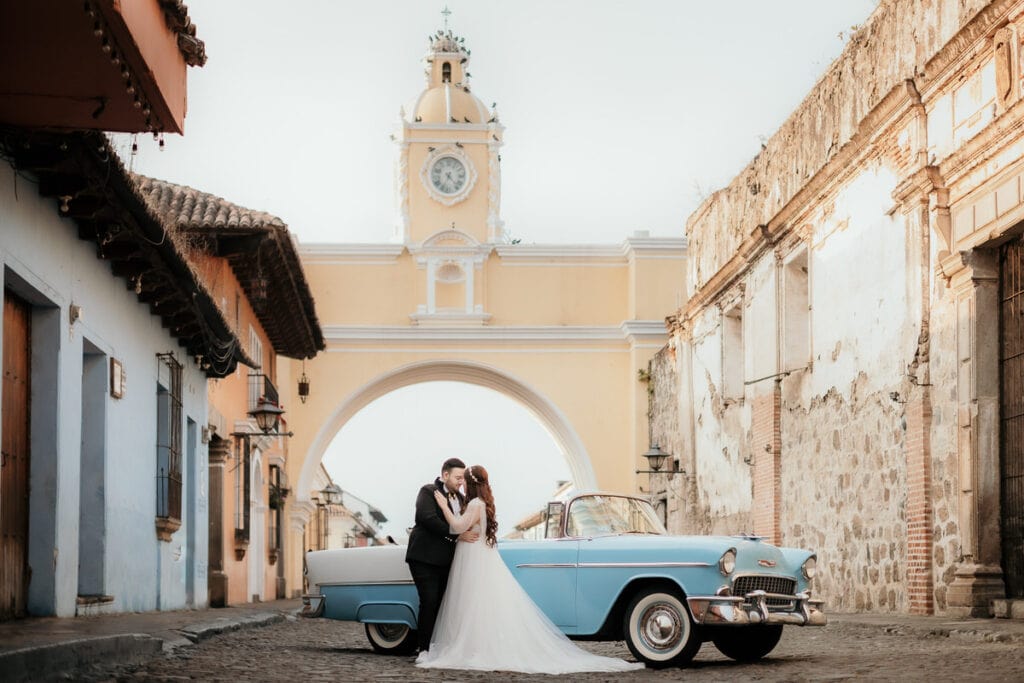 pareja en arco de Antigua Guatemala junto a automovilistas antigua en sus fotos de boda.
